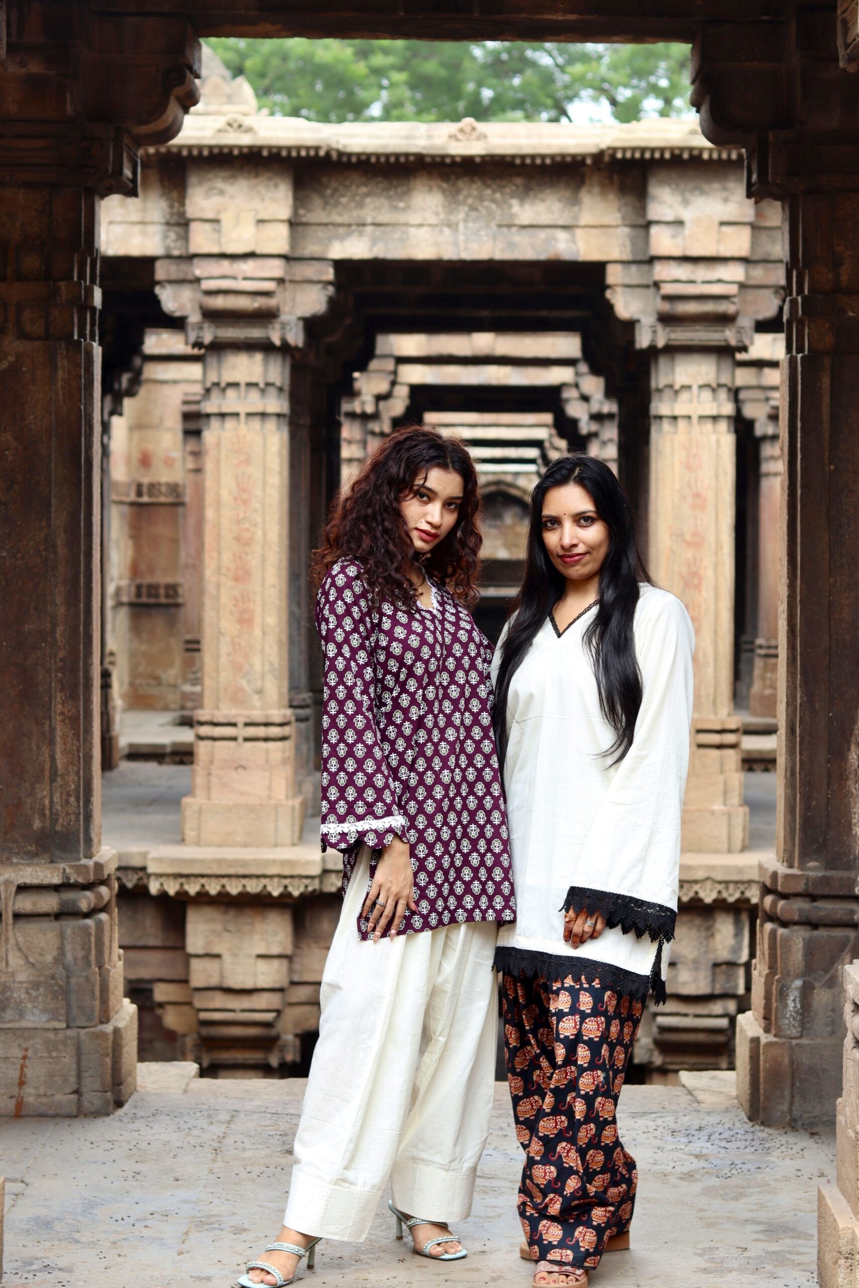 Two women in elegant traditional outfits at a historic stepwell, showcasing cultural fashion.